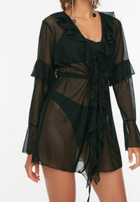 Black sheer cover-up dress with ruffled sleeves and front tie detail. Features a lightweight, flowing fabric and a semi-transparent design.
