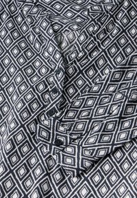 Knapp-up skjorta i marinblått och vitt med ett geometriskt diamantmönster; har en krage och knappslå med svarta knappar. Mjuk textur.