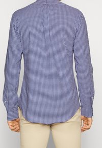 Košile s dlouhým rukávem v námořnické a bílé kostkované vzoru, vyrobená z lehkého materiálu s límečkem na knoflíky a zakřiveným lemem.