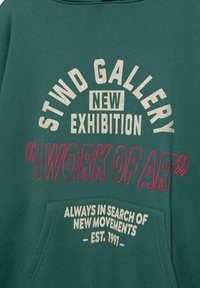 Felpa verde con testo curvo bianco e rosa: "STWD GALLERY NUOVA MOSTRA 'UN CAPOLAVORO'" con tasca frontale e dettagli a costine.