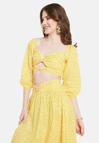 Completo a due pezzi giallo a quadretti con maniche a sbuffo, design con ritagli e accenti rosa. Composto da un tessuto leggero con un motivo testurizzato.