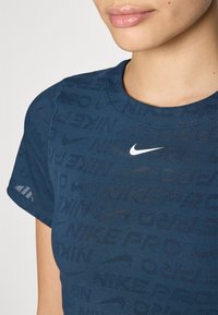 T-paita tummansinisestä pehmeästä kankaasta, jossa on teksturoitu kuvio ja "NIKE PRO" eri sävyissä, valkoisen Nike-logon korostamana.