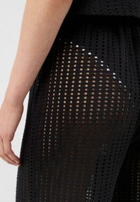 Tejido negro texturizado con un diseño de malla, con secciones abiertas que crean un efecto de patrón. Primer plano de una zona ajustada cerca de la cintura.