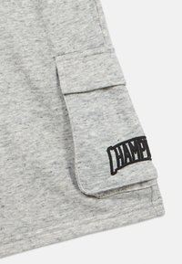 Γκρι ύφασμα ελαφρώς μαρλεμένο, μπλουζάκι με τσέπη και κεντημένο μαύρο λογότυπο "CHAMPION" στο πλάι. Καθημερινό σχέδιο με κοντά μανίκια.