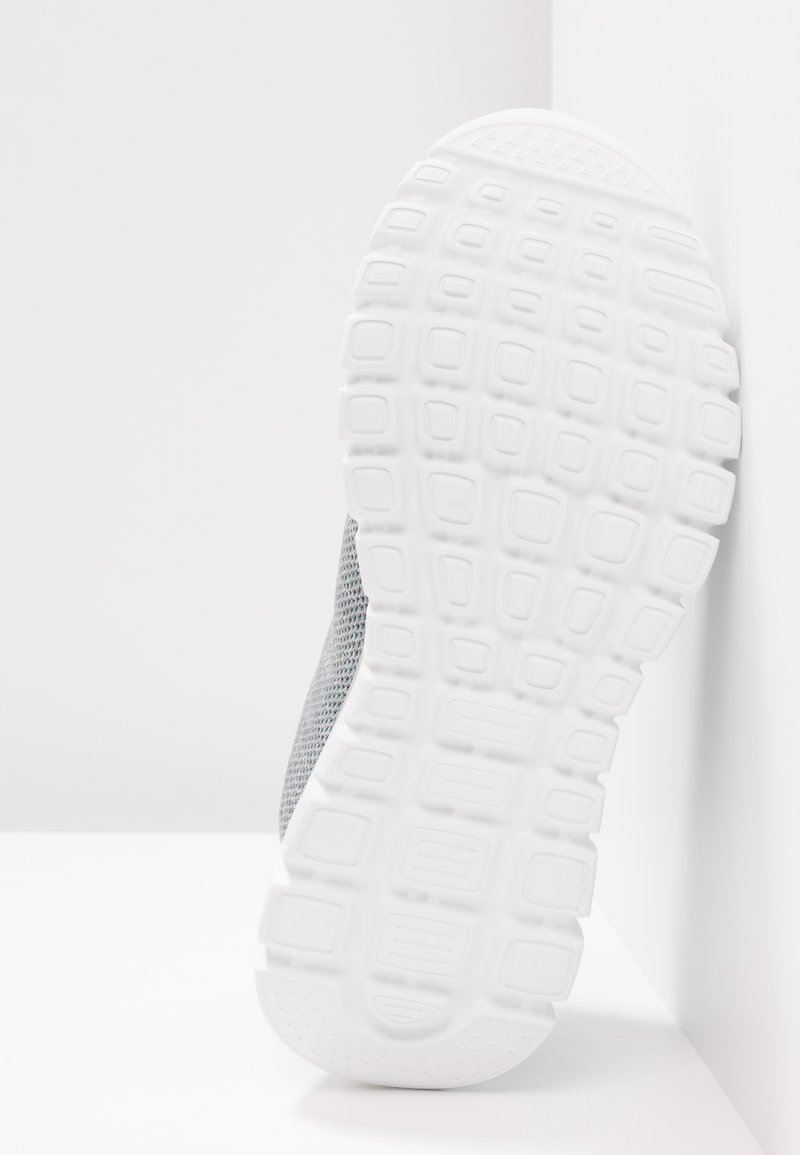 Suela de zapato deportivo gris con una suela de goma blanca texturizada, que presenta ranuras profundas y elementos de amortiguación para agarre y comodidad.