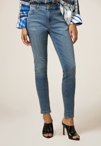 Vaqueros skinny de un azul claro, confeccionados en denim, con una cintura de altura media y un ligero desgastado. Combinados con unos tacones altos negros de punta abierta.