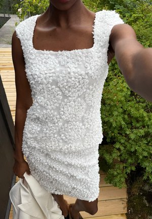 Abito bianco dal design testurizzato con motivi floreali arricciati e scollatura quadrata, silhouette aderente, senza maniche e gonna arricciata.