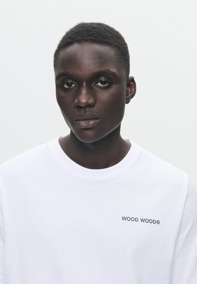 Vit bomullströja med varumärket "WOOD WOOD" i svart på vänster bröstområde. Rund halsringning och normal passform.