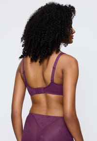 Lila bh med en slät textur, justerbara band och en hak-och-öga-stängning på baksidan. Blommönster pryder tyget.