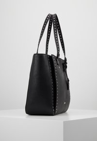 Sac fourre-tout en similicuir noir avec des anses cloutées, des côtés effilés et une finition texturée. Doté de détails métalliques et d'une petite étiquette.
