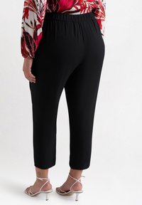 Pantaloni neri cropped con una vita elasticizzata, texture liscia e un fit rilassato, abbinati a sandali bianchi con tacco.