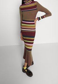 Abito midi a coste con strisce verticali multicolori in borgogna, viola, verde e marrone. Presenta un colletto alto e un orlo svasato. Scarpe con plateau nere.