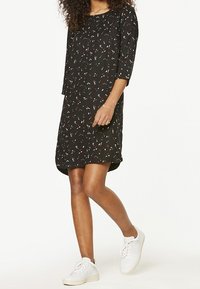 Czarna sukienka z rękawami do trzech czwartej, zdobiona rozproszonym wzorem w kolorze białym, czerwonym i niebieskim. Noszona z białymi trampkami. Gładki materiał.