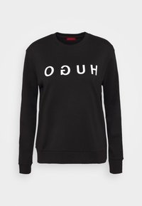 Sweat-shirt noir à manches longues avec col rond et texte blanc inversé "HUGO" sur la poitrine sur un fond uni.