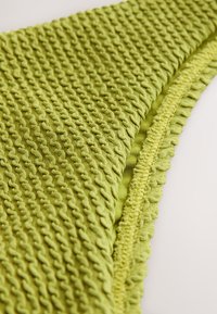 Tela verde texturizada con un diseño acanalado y borde ondulado, que presenta un acabado suave y tejido. Ideal para uso cómodo o decoración.