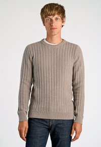 Ljusgrå kabelstickad tröja med långa ärmar och rund halsringning, i kombination med mörka jeans. Tröjan har ribbade mudd och nederkant.