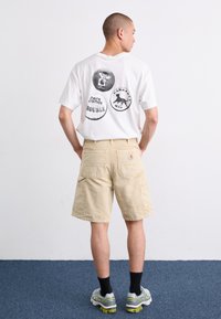 White graphic t-shirt with circular prints, beige cargo shorts, and gray athletic shoes. Visible pockets on shorts and black socks.