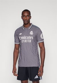 Maglia da calcio grigia con un motivo testurizzato, caratterizzata da un logo bianco e dal testo "Emirates Fly Better", e colletto e maniche a righe. Pantaloni corti neri.