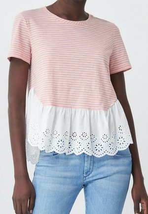 Kobieta ubrana w jasnoróżową i białą bluzkę z krótkim rękawem z poziomymi paskami i obszyciem z koronki ażurowej, w połączeniu z niebieskimi dżinsami.