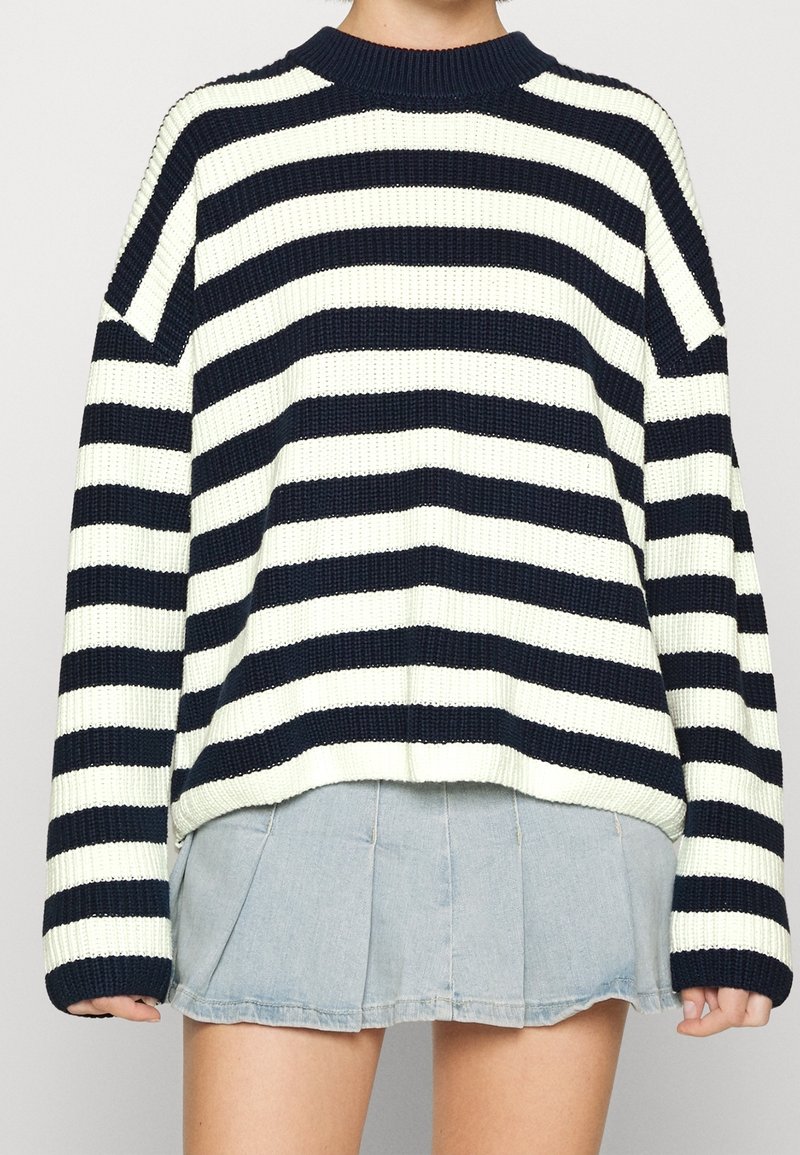 Stickad tröja med marinblå och krämfärgade ränder, rund halsringning och sänkta axlar. Kombinerad med en ljus jeanskjol. Texturerat tyg.