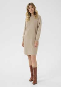 Beige garš piedurkņu kleita ar brīvu piegriezumu, ar aprocēm, apakšējā daļa līdz ceļiem, kopā ar brūnām zamšādām augstām zābakiem.