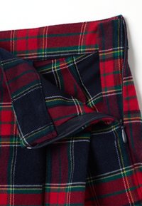 Tessuto tartan rosso, blu navy e verde con una cerniera nera parzialmente aperta, che mostra strati di plaid sovrapposti.