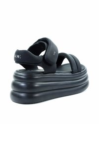 Czarne platformy na sandały z warstwową, zaokrągloną podeszwą. Wykonane z teksturowanego materiału, z szerokimi paskami i zapięciem na rzep w okolicy kostki.