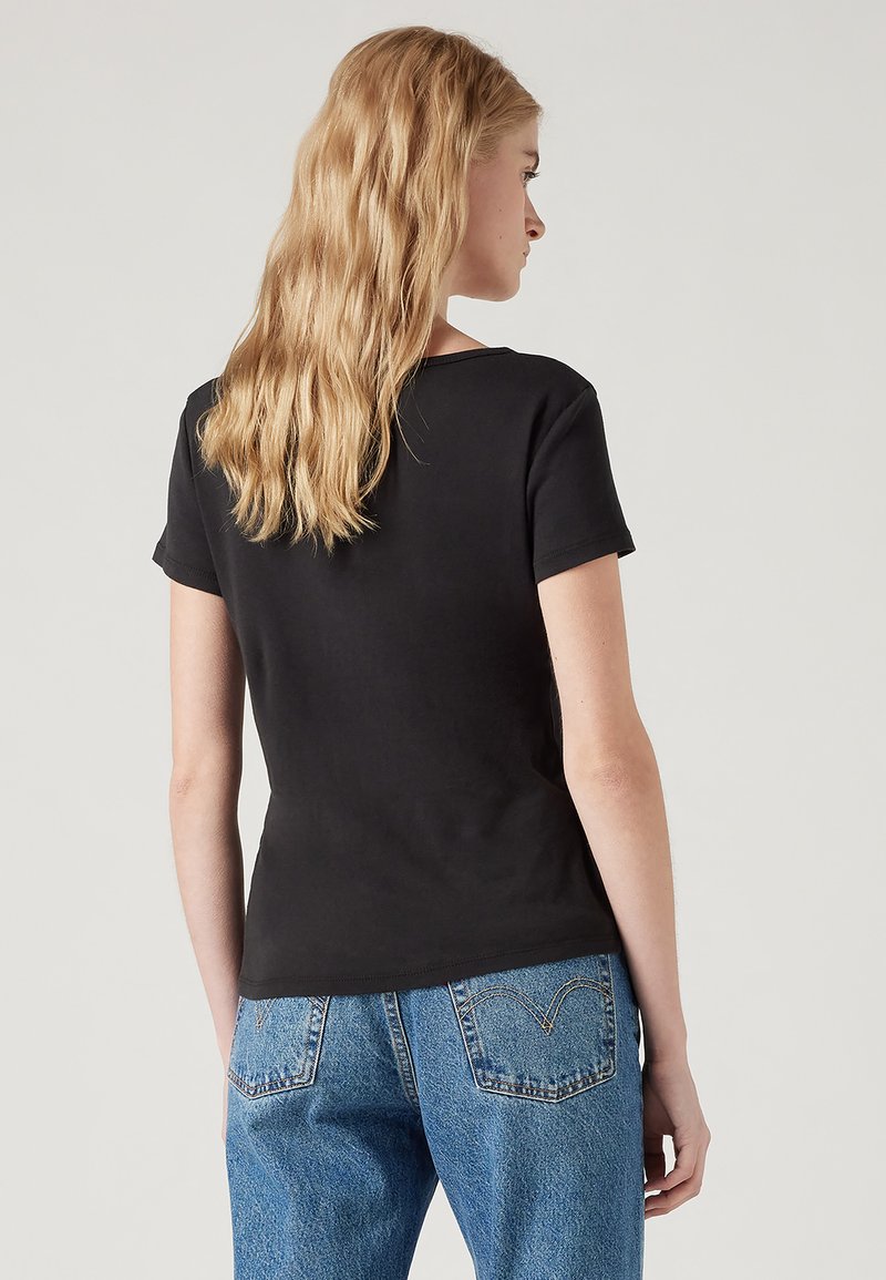 Camiseta negra de manga corta con cuello redondo, hecha de algodón. La parte de atrás presenta una textura suave con un corte ajustado. Combinada con jeans de mezclilla.