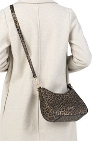 Manteau beige porté avec un sac bandoulière à imprimé léopard, doté de quincaillerie dorée et d'une sangle réglable reposant sur le dos.