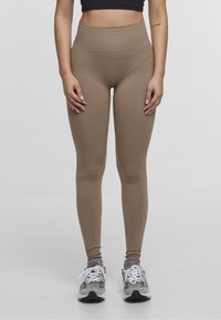 Leggings ajustados de talle alto en color beige, fabricados en una tela suave y elástica. Combinados con zapatillas deportivas grises.