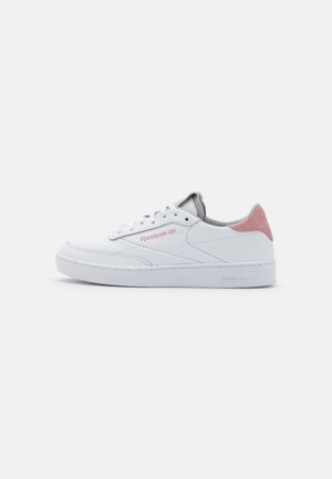 Baskets basses blanches Reebok avec un accent rose clair au talon et un logo rose sur le côté, lacets blancs et semelle en caoutchouc blanche.