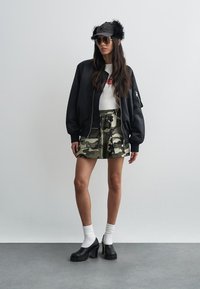 Μαύρο μπουφάν τύπου βομβαρδιστικού, λευκό εφαρμοστό τοπ, σορτς παραλλαγής, μαύρα παπούτσια με πλατφόρμα, λευκές κάλτσες και μαύρο καπέλο από ψεύτικη γούνα με γυαλιά ηλίου.