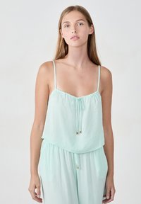 Camiseta sin mangas de un suave color verde menta con tirantes finos y cordón ajustable. Tejido suave y fluido con un corte relajado y delicados acentos dorados.