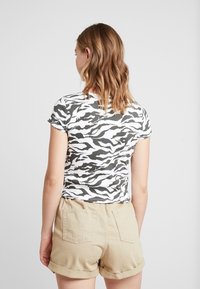 Tričko s krátkým rukávem s bílým a černým zebra vzorem, doplněné béžovými zkrácenými šortkami vyrobenými z měkké látky.