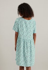 Korte mouw, knielange jurk in lichtblauw met een abstract patroon van zwarte, groene en witte vormen; gemaakt van zachte stof.