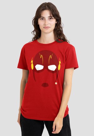 Young woman wearing red t-shirt with stylized superhero mask graphic featuring yellow lightning bolts and white eye shapes.
