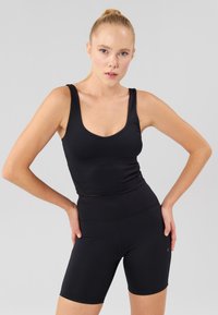 Parte superiore sportiva nera con spalline larghe e scollatura a girocollo, abbinata a pantaloncini neri a vita alta. Tessuto morbido, design aderente.