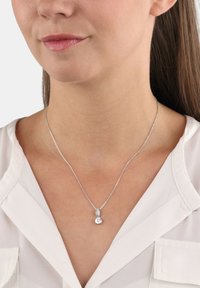 Collar de plata que presenta un colgante redondo y transparente con un acento en forma de lágrima, exhibido en el cuello de una mujer contra un fondo de blusa clara.