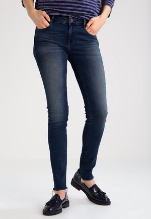 Jeans ajustados de color azul oscuro, hechos de denim con una textura suave, de cintura alta, y Diseño estándar de cinco bolsillos, combinados con zapatos negros de cordones.