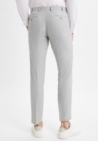 Hellgraue maßgeschneiderte Hose aus strukturiertem Stoff. Mit einem figurnahen Schnitt, zwei Gesäßtaschen mit Knopfverschlüssen und einer schmalen Beinform.