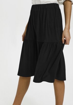 Sort midi-nederdel lavet af blødt stof, med elastisk taljebånd og lagdelt design med kontrasterende teksturerede paneler.