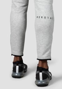 Grå atletiske joggers har en tætsiddende pasform med et sort logo, manchetter ved anklerne og kontrasterende sort kant. Kombinationen er med sorte og grå sneakers.