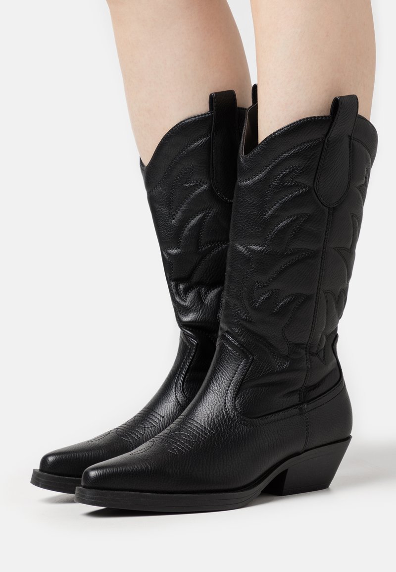 Botas de cowboy de cuero negro con punta afilada, costuras decorativas en el caña y un tacón bajo apilado para mayor estabilidad.