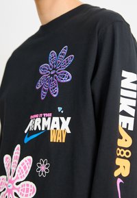 Svart långärmad t-shirt med färgglada blommönster, logotext i vitt och orange, rund halsringning och ribbade ärmmuddar.