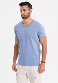 Světle modré tričko s výstřihem do V a krátkými rukávy; měkká, hladká textura; přiléhavý střih; spárované s béžovými cargo kalhotami a tmavým náramkem.