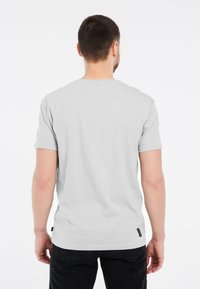 Lichtgrijze t-shirt van katoen, met korte mouwen, ronde hals en een klein zwart merklabel aan de onderrand aan de linkerkant.