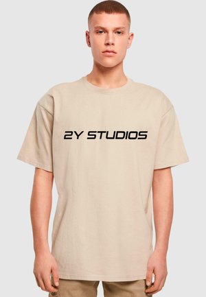 Beige, oversize pamut póló rövid ujjakkal és kerek nyakkivágással. Fekete "2Y STUDIOS" logó nyomva az elején.