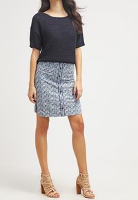 Knit navy sweater with short sleeves paired with a patterned skirt featuring blue and green circles, complemented by beige strappy heels.