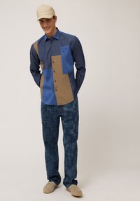 Blue and beige color-block shirt with long sleeves, buttons, and a chest pocket, paired with textured blue patterned pants and beige shoes.