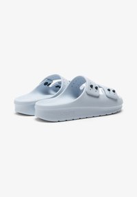 Light blue rubber slip-on sandals featuring a wide strap, ventilation holes, and a textured sole. Company logo embossed on the side.